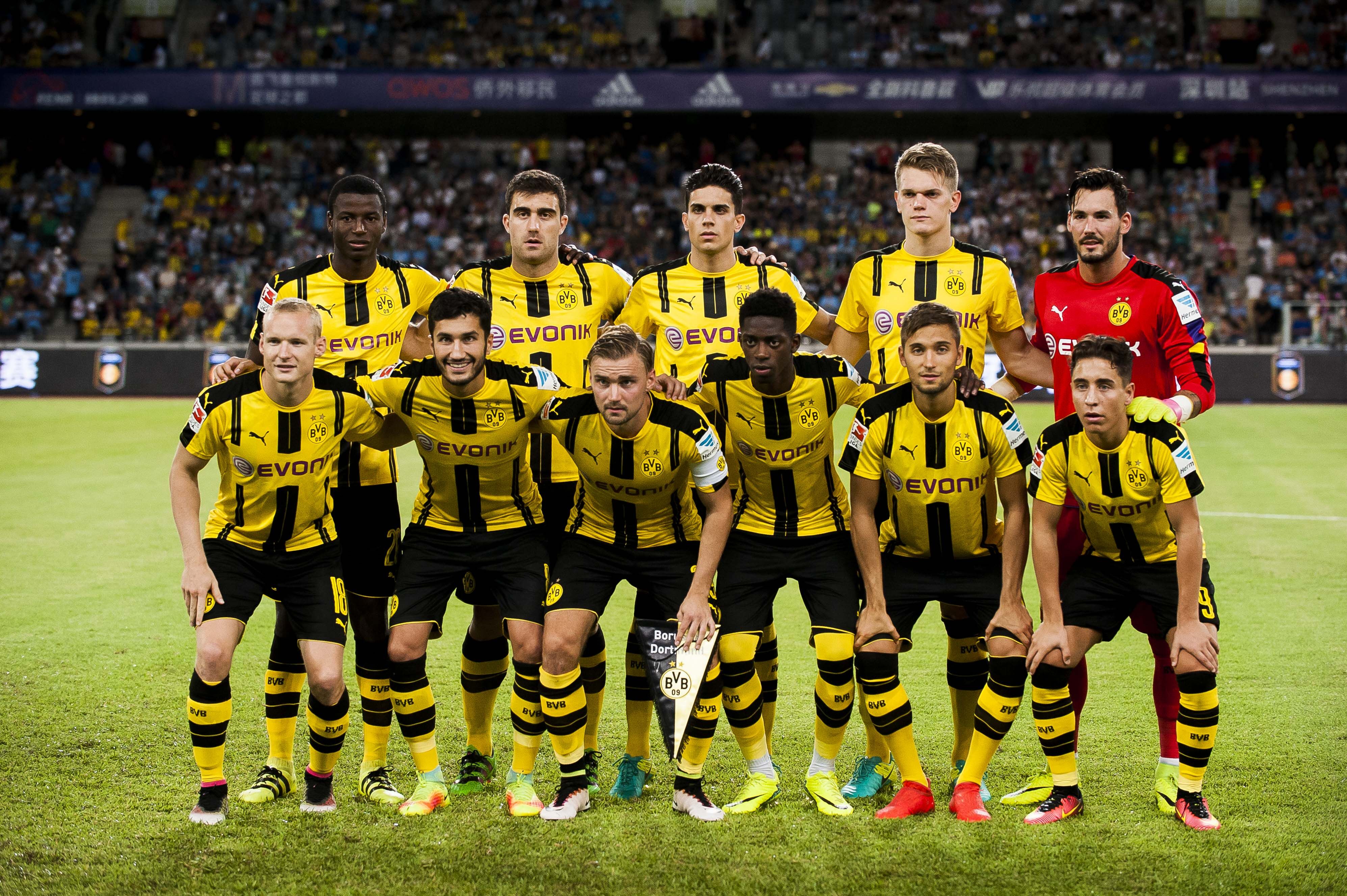  The image shows the starting lineup of Borussia Dortmund players in a soccer match, all wearing yellow jerseys and black shorts, standing in a row with determination on their faces.